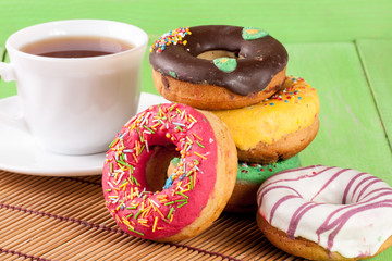 pile of glazed donuts with a cup of tea on a green wooden background