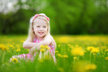 Adorable little girl in blooming dandelion meadow on beautiful spring day