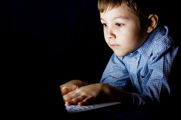 Little boy doing homework on the computer in the dark night. Child to play the game on a laptop.