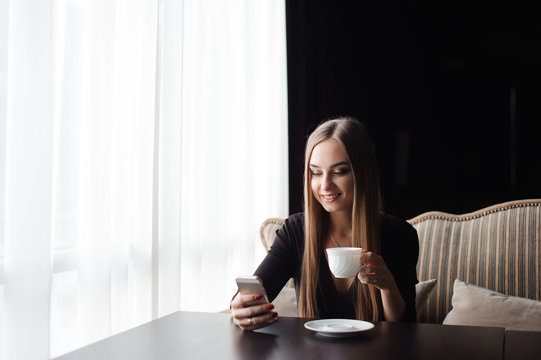 Young woman drinking coffee in a cafe and using a mobile phone