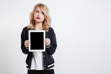 Thoughtful young lady showing display of tablet computer