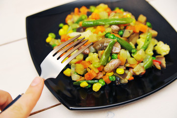 Black plate with a vegetable saute on a white wooden background