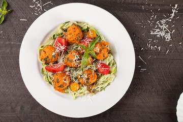Oven roasted sweet potato balls on sautéed zucchini on dark wooden background far away shot