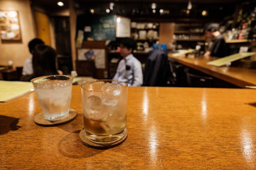Cocktail on the bar with glass of ice and customers in the background