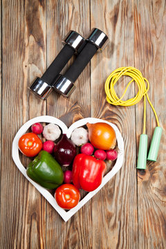 Sport and diet. Vegetables  dumbbells. Peppers, tomatoes, garlic, onions,  radishes in the heart on rustic background