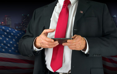 Closeup of a United States of America politician with red neck tie and American flag lapel pin texting on his cell phone.