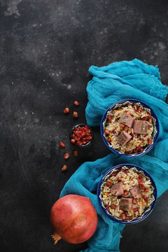 Pilaf with beef and pomegranate seeds on a dark metal background, flat-lay with copy space