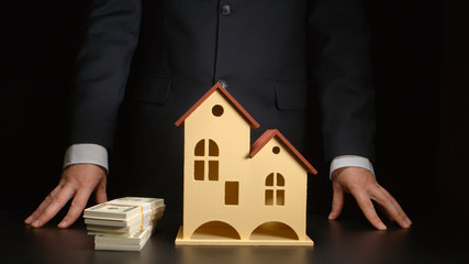 Businessman stands near a money on a table with a house model