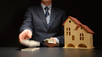 Businessman counts a money and near a house model on a table