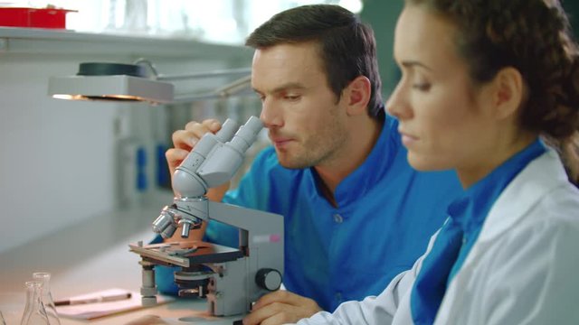 Doctors team working in lab. Close up of lab medical man and woman talking. Closeup of scientist working in medical laboratory. Lab scientist working with microscope and tablet pc