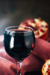 Fresh pomegranate wine in glass on black rustic surface.