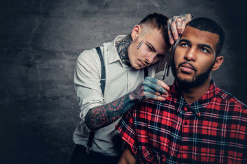 Tattooed barber cuts the beard to a Black bearded male.