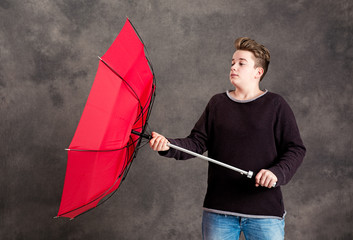 teenager with red umbrella standing in strong breeze