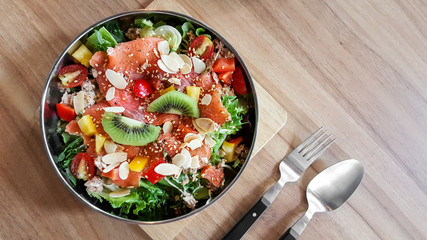 Homemade smoked salmon fruit salad with spoon and fork on natural wood table.