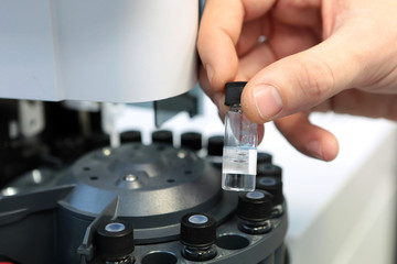 People hand holding a test tube vial sets for analysis in the gas liquid chromatograph. Laboratory assistant inserting laboratory glass bottle in a chromatograph vial