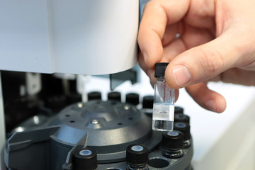 People hand holding a test tube vial sets for analysis in the gas liquid chromatograph. Laboratory assistant inserting laboratory glass bottle in a chromatograph vial