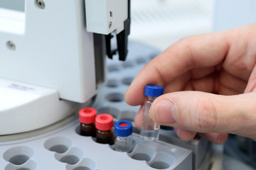 People hand holding a test tube vial sets for analysis in the gas liquid chromatograph. Laboratory assistant inserting laboratory glass bottle in a chromatograph vial