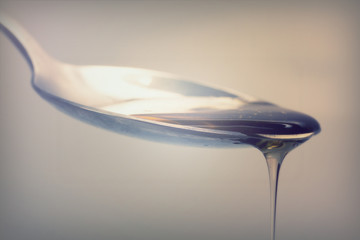 Honey pouring from spoon against a light background