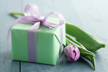green gift box with purple bow and tulip on blue wood background, romantic photo