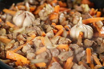 frying pork meat with carrot, onion and garlick for pilaf, closeup macro