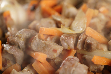 frying pork meat with carrot, onion and garlick for pilaf, closeup macro