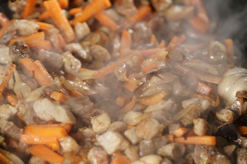 frying pork meat with carrot, onion and garlick for pilaf, closeup macro