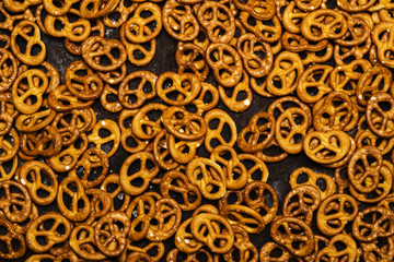 Background texture of crispy mini pretzels with large salt crystals on a dark metallic background 