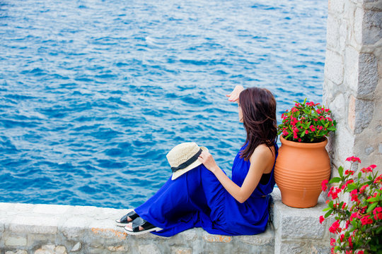 photo of beautiful young woman sitting near ot with flowers on the sea background