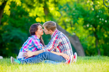 Naklejka na ściany i meble beautiful cute couple sitting on the field and going to kiss on the trees background