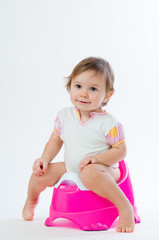 Little smiling girl sitting on a pot. Isolated on white background.