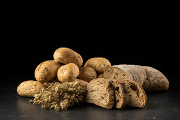 Oat bunch, baked white bread isolated on black background. Grain bouquet, golden oats spikelets and buns on dark wooden table. Food, bakery concept
