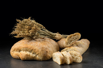 Baguette and ciabatta, bread slices on dark wooden table. Wheat and fresh mixed breads isolated on black background. Food, bakery concept