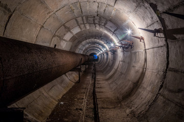 Old round dirty underground technical tunnel of heating duct with rusty pipeline