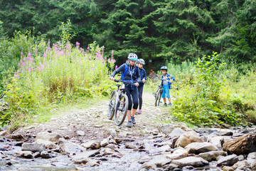 Young woman with her children on bikes wade the mountain creek