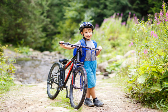 Small smiling boy in helmet standing with bicycle on mountain trail