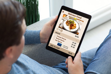 man in jeans holding tablet computer with app delivery food