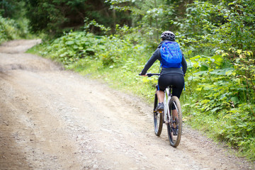 Fototapeta na wymiar Young woman with backpack riding bicycle on mountain road in the forest