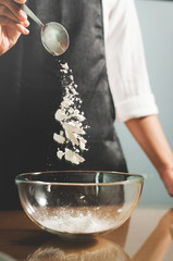 Woman chief sprinkling flour into glass bowl.