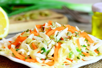 Delicious vegetable salad on a plate. Homemade salad with white cabbage, carrots, green onions, pumpkin seeds, lemon juice and olive oil. Easy diet food. Closeup