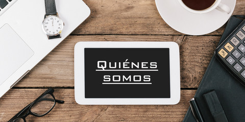 Quienes somos, Spanish text for About Us on screen of tablet computer at office desk