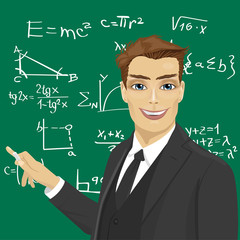 young male math teacher with piece of chalk standing next to blackboard