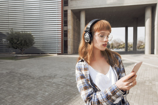 portrait of a young yoman that is using a music application in her smart phone device, while in a modern urban, city architecture environment 