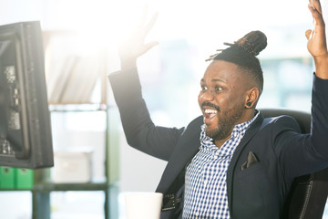 African American office worker with collected rasta hair exulting reading good news on his computer