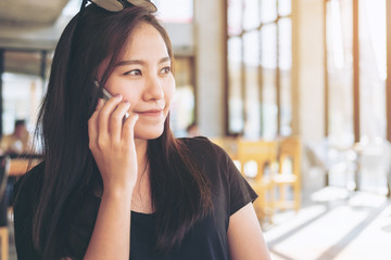 A beautiful Asian girl talking on smart phone with smiley face in modern cafe