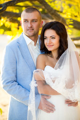 Portrait of Couple of lovers newlyweds on nature. Brunette bride in wedding dress with a beautiful hairstyle, veil and makeup and her husband in a suit