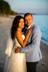 Portrait of Couple of lovers newlyweds on the seafront. Brunette bride in wedding dress with a beautiful hairstyle, veil and makeup and her husband