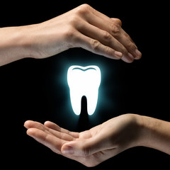 Isolated image of two hands on black background. Tooth icon in the center, as a symbol of dental...