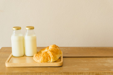 fresh croissant and two bottles of milk on wooden tray on wooden table in the morning