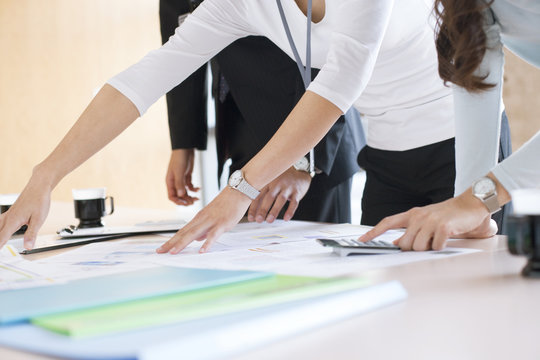 Mid section of business people discussing with blueprint in meeting