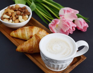 Cup of cappuccino, croissants, flowers and bowl of nuts with on the table